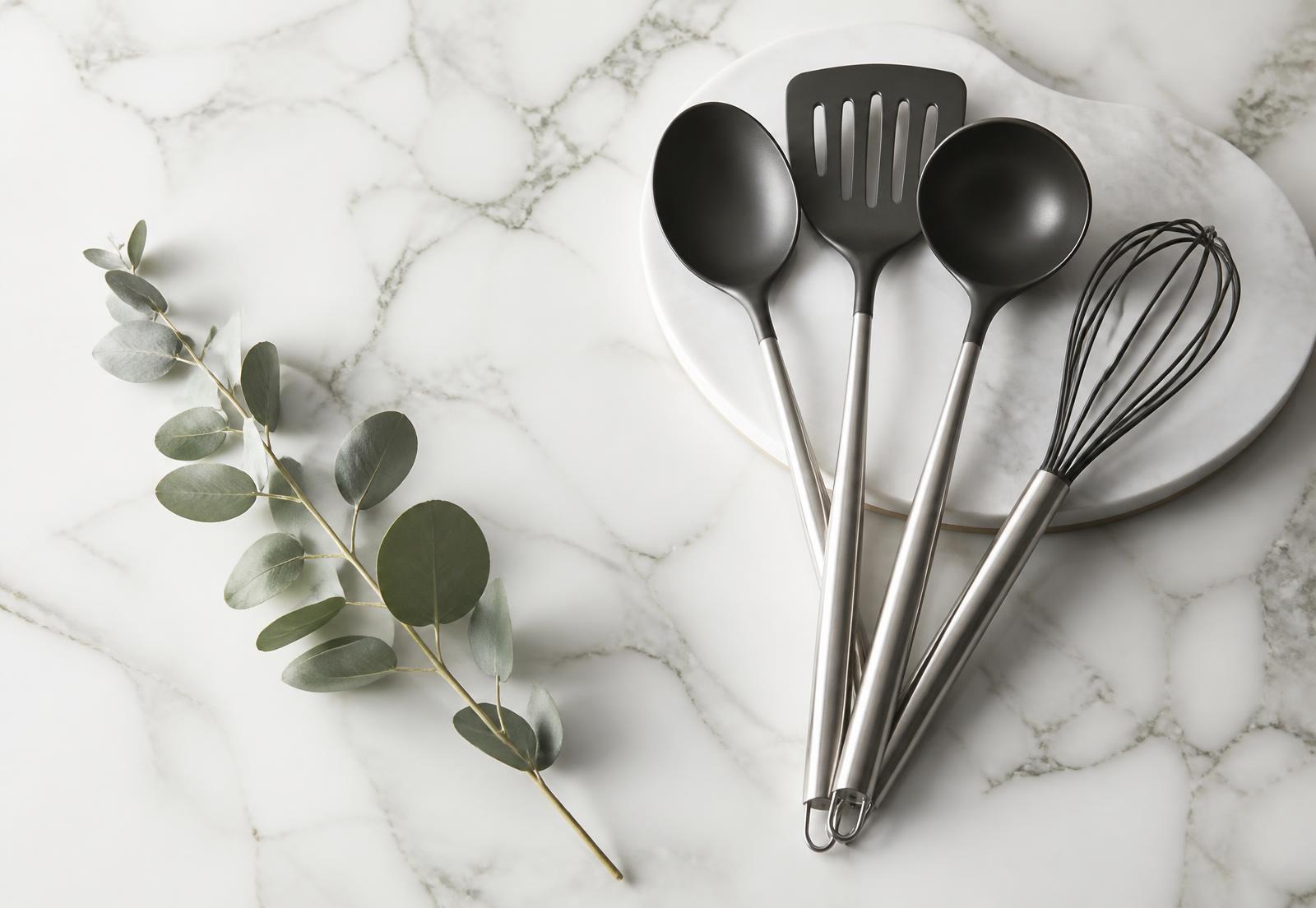 Utensílios de cozinha em aço escovado e preto fosco sobre mármore branco